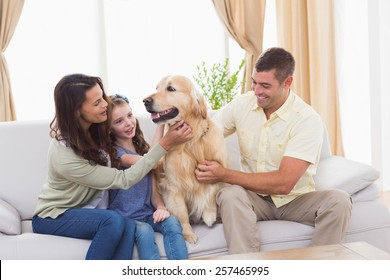 Loving Family Stroking Dog While Sitting On Sofa At Home