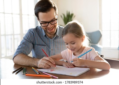 Loving father   adorable little daughter drawing colorful pencils in album  sitting at desk at home  happy dad wearing glasses   preschool girl spending leisure time weekend together