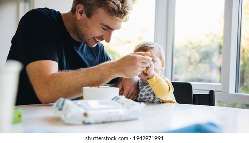Loving father feeding his baby with a spoon while on paternity leave. Man spoon feeding his little baby during paternity leave.