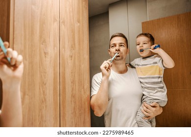 A loving father is holding his son in the arms and brushing their teeth together in a bathroom. - Powered by Shutterstock