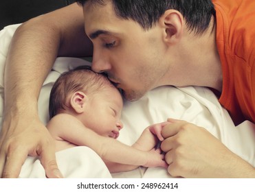 Loving Father Kissing His New Born Baby.Father Kissing His Baby Boy Forehead While His Sleeping And Holding Hands. Parent Love.