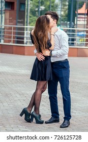 a loving girl in a short black dress kisses and hugs her man in a suit in the park - Shutterstock ID 726125728