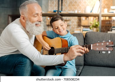 Loving grandfather teaching grandson how to hold guitar