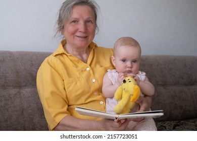 Loving grandmother reading a book to baby girl holding book sitting on sofa. Nanny granny telling story to a grandchild - Shutterstock ID 2157723051