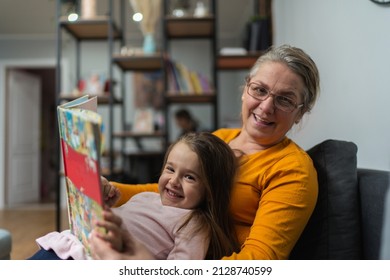 Loving grandmother teaching granddaughter holding book sitting on sofa, grandma baby sitter embracing kid girl reading fairytale to cute child, nanny granny telling story to preschool grandchild - Powered by Shutterstock