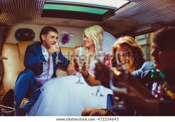 Loving groom looks at a bride with love while\
drinking champagne in the\
limousine