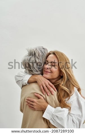 Loving grownup daughter hug embrace old mother feel grateful and thankful, isolated on white studio background. Caring adult child cuddle mature mom. Vertical narrow shot. Motherhood.