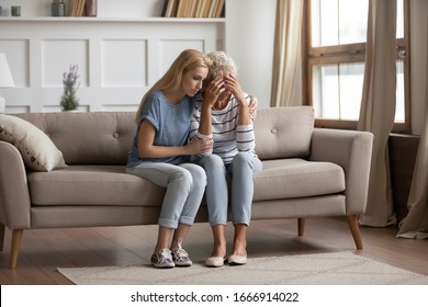 Loving Grownup Daughter Sit On Couch In Living Room Hug Support Upset Depressed Senior Mother, Caring Adult Young Woman Child Embrace Sad Crying Mature Mom, Comfort And Caress Parent At Home