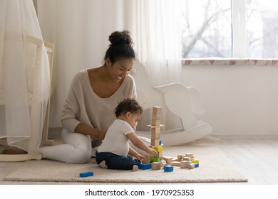 Loving happy young African American mother play with blocks brick with small toddler baby child. Caring ethnic mom have fun engaged in game activity with little daughter kid. Motherhood concept.