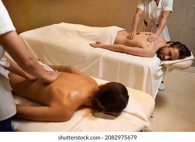 Loving heterosexual couple of handsome man and beautiful woman relaxing on a massage table during back massage performed by two professional masseuses in luxury spa clinic. Ayurveda, body care concept
