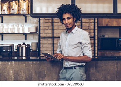 Loving his small business. Young cheerful African man using digital tablet and looking at camera with smile while standing at bar counter - Shutterstock ID 393539503