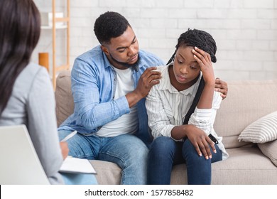 Loving husband supporting his depressed wife during psychotherapy session with counselor, free space