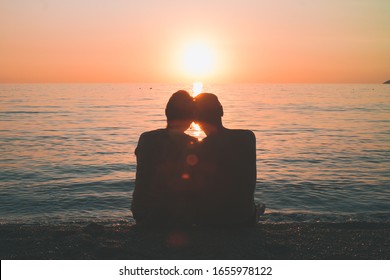 Loving husband and wife sit at sunset by the sea, old people enjoy the sunset together