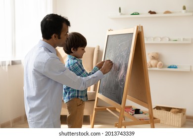 Loving Indian Father With Little Son Drawing On Black Board With Colored Chalks Together, Painting, Young Dad And Preschool Boy Child Having Fun At Home, Family Involved In Creative Activity