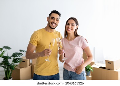 Loving interracial spouses celebrating moving day with champagne, toasting in new apartment among cardboard boxes. Happy millennial married couple moving into their own home - Powered by Shutterstock