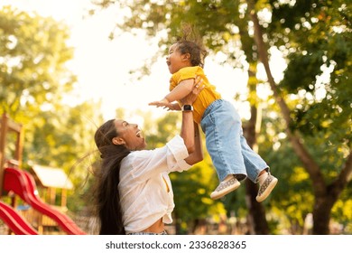 Loving japanese mom lifting her little daughter up in air while spending time together in green park at outdoor playground. Millennial asian mother playing with toddler girl holding kid in arms - Powered by Shutterstock