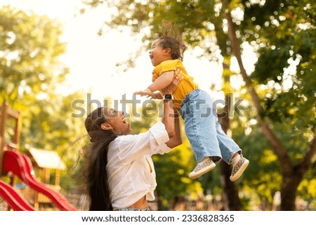 Loving japanese mom lifting her little daughter up in air while spending time together in green park at outdoor playground. Millennial asian mother playing with toddler girl holding kid in arms