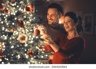 A loving joyful young adult couple decorating the Christmas tree together on cozy Christmas Eve at home. - Powered by Shutterstock