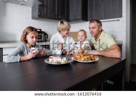 Loving kind smiling parents mom and dad feed their little cute children their sister and brother with a morning breakfast in a cozy spacious kitchen. Concept of good relations between relatives