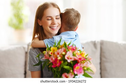 Loving Little Son Hugging Happy Mom And Greeting With Bouquet Of Alstroemerias During Mothers Day Celebration At Home