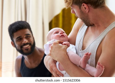 Loving Male Same Sex Couple Cuddling Baby Daughter At Home In Garden Together