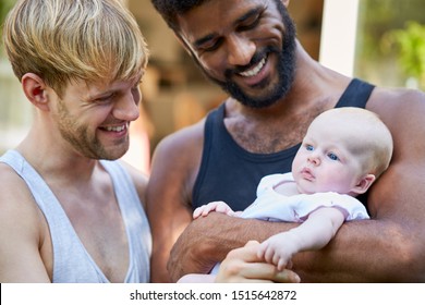 Loving Male Same Sex Couple Cuddling Baby Daughter At Home In Garden Together