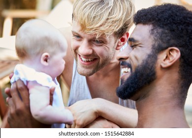 Loving Male Same Sex Couple Cuddling Baby Daughter At Home In Garden Together