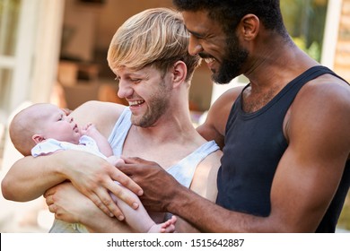 Loving Male Same Sex Couple Cuddling Baby Daughter At Home In Garden Together