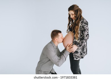 A loving man gently kisses the big belly of a pregnant woman on a white background cyclorama, photo studio. Photography, concept.