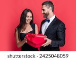 Loving man giving present gift box for Valentines day to surprised woman. Man receiving present. Happy Valentines day. Couple in love isolated on red. Birthday couple with gift. I love you