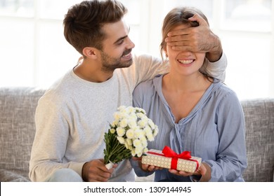 Loving man husband boyfriend with flowers closing eyes of woman girlfriend holding gift box guessing present making romantic surprise to wife, couple celebrating Valentines day anniversary birthday - Powered by Shutterstock