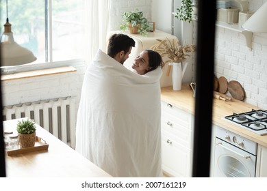 Loving man and woman standing in modern kitchen wrapped together in blanket smile look at each other enjoy conversation, above view. Romantic weekend, affection, relocation and cohabitation concept