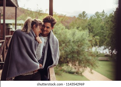 Loving man and woman standing in their hotel room balcony wrapped in blanket. Romantic couple in a blanket standing together on a winter holiday. - Powered by Shutterstock