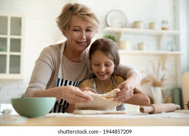 Loving mature Caucasian 60s grandmother roll dough bake bread or sweet buns with happy little granddaughter in kitchen. Elderly grandparent cooking pie or cookies with small grandchild at home. - Powered by Shutterstock