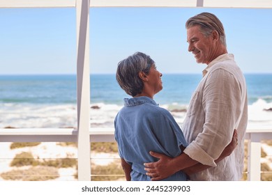 Loving Mature Couple Hugging In Beachfront House Overlooking Ocean For Summer Vacation - Powered by Shutterstock