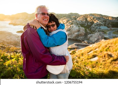 Loving mature couple traveling, standing on the top of rock, exploring. Active man and woman hugging and kissing, Happily smiling. Scenic view of mountains and sea on sunset. Norway, Lindesnes - Powered by Shutterstock