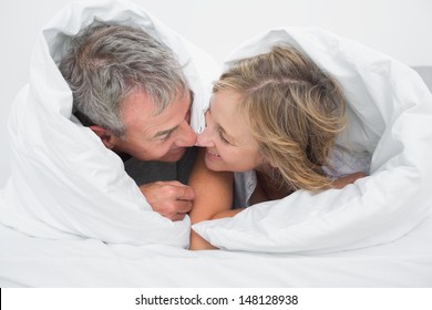 Loving Middle Aged Couple Under The Duvet Rubbing Noses In Bedroom At Home