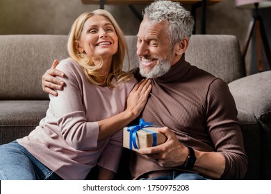 Loving middle aged man making surprise by giving gift in box to his wife celebrating anniversary or birthday at home - Powered by Shutterstock