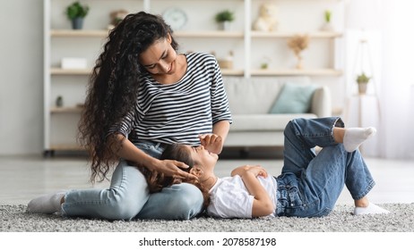 Loving middle eastern long-haired millennial lady bonding with her kid at home, sitting on floor and caressing laying on her laps happy preschool girl, living room interior, panorama with copy space - Powered by Shutterstock