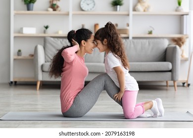 Loving middle eastern mother and daughter in sportswear working on abs together, exciting little girl holding her mom legs while she doing crunches, touching each other with foreheads, home interior - Powered by Shutterstock