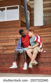 Loving Middle-aged Black Father With American Flag On Shoulders Sitting On Bleacher Bench And Embracing Son While Talking To Him