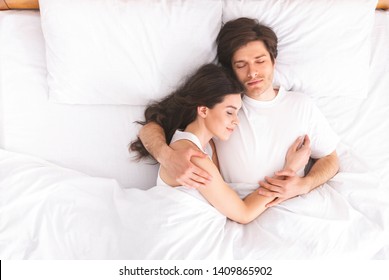 Loving millennial couple sleeping in bed in morning and hugging, love and relationships concept, top view, free space