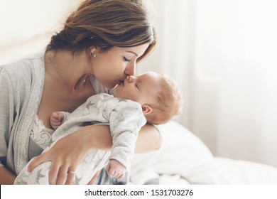 Mãe amorosa cuidando de seu bebê recém-nascido em casa. Retrato brilhante de mãe feliz segurando criança infantil nas mãos. Mãe abraçando e beijando seu filho pequeno de 2 meses.