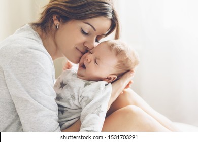 Loving mom carying of her newborn baby at home. Bright portrait of happy mum holding sleeping infant child on hands. Mother hugging her little 2 months old son.