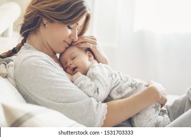 Любящая мама ухаживает за новорожденным ребенком дома. Яркий портрет счастливой мамы, держащей спящего ребенка на руках. Мать обнимает своего маленького двухмесячного сына.