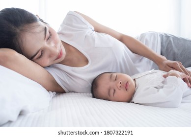 Loving mom carying of her newborn baby at home. Bright portrait of happy mum holding sleeping infant child on hands. Mother hugging her little. Mother and her baby son, sleeping on a big bed.