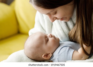 Loving mom carying of her newborn baby at home over window lighting. Woman holds and hugs her child. Bright portrait of happy mum holding sleeping infant child on hands.