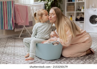 Loving Mom Takes Care Of Little Adorable Daughter, Little Girl Helps Woman Sort Clothes For Laundry, Baby Sits In Bowl Gives Kiss To Beloved Mother.