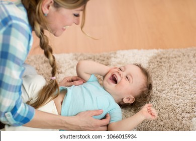 Loving mom tickling her little baby kid on carpet at home