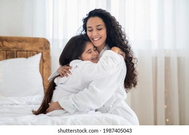 Loving mother and daughter in bathrobes embracing while spending time together at home, copy space. Happy young woman hugging her little girl, closing eyes, enjoying beauty day